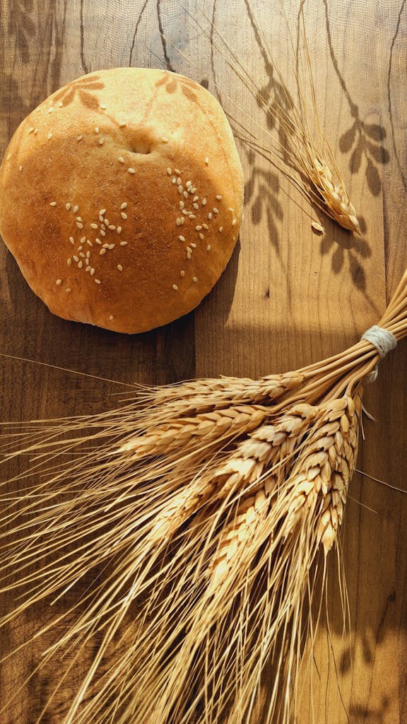 A round loaf of sesame-seed bread with wheat stalks on a wooden table, lit by warm sunlight for gluten intolerance article