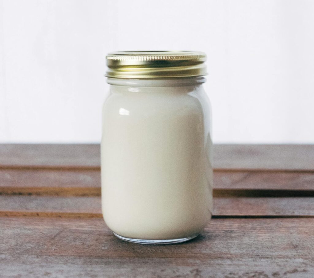 A rustic glass jar filled with creamy yogurt, placed on a wooden table. Ideal for healthy food themes.