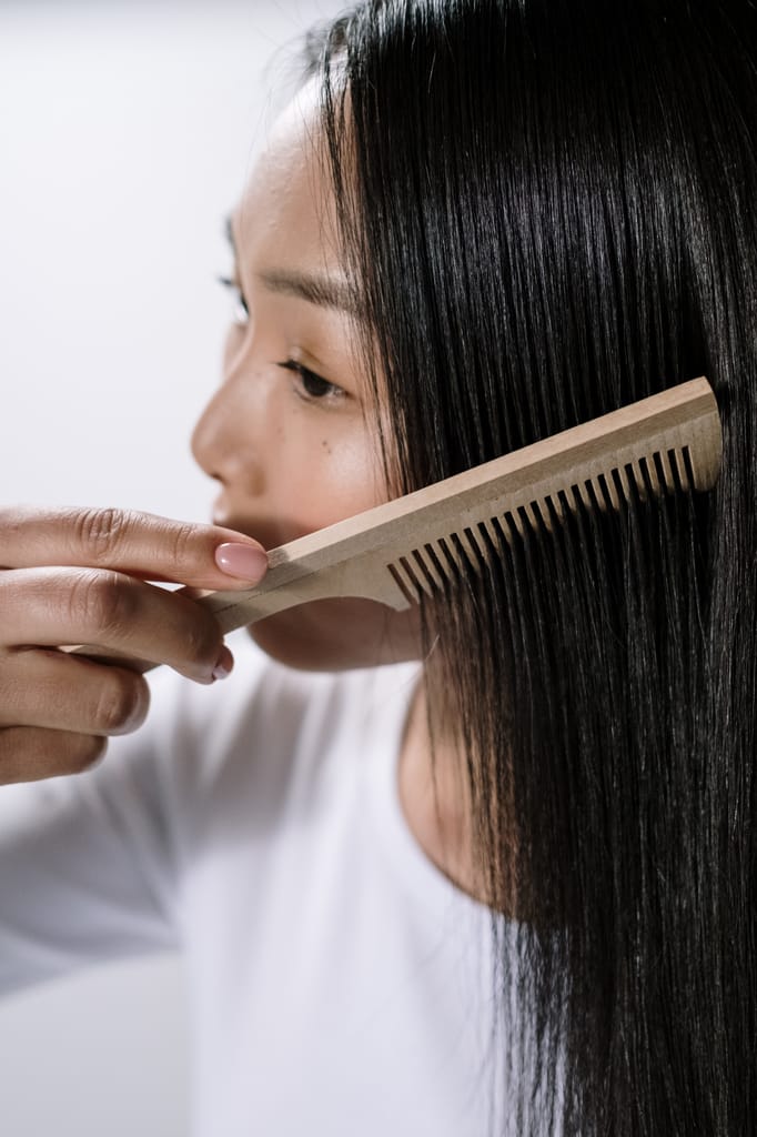 Close-up of an Asian woman using a wooden comb to style her hair indoors.