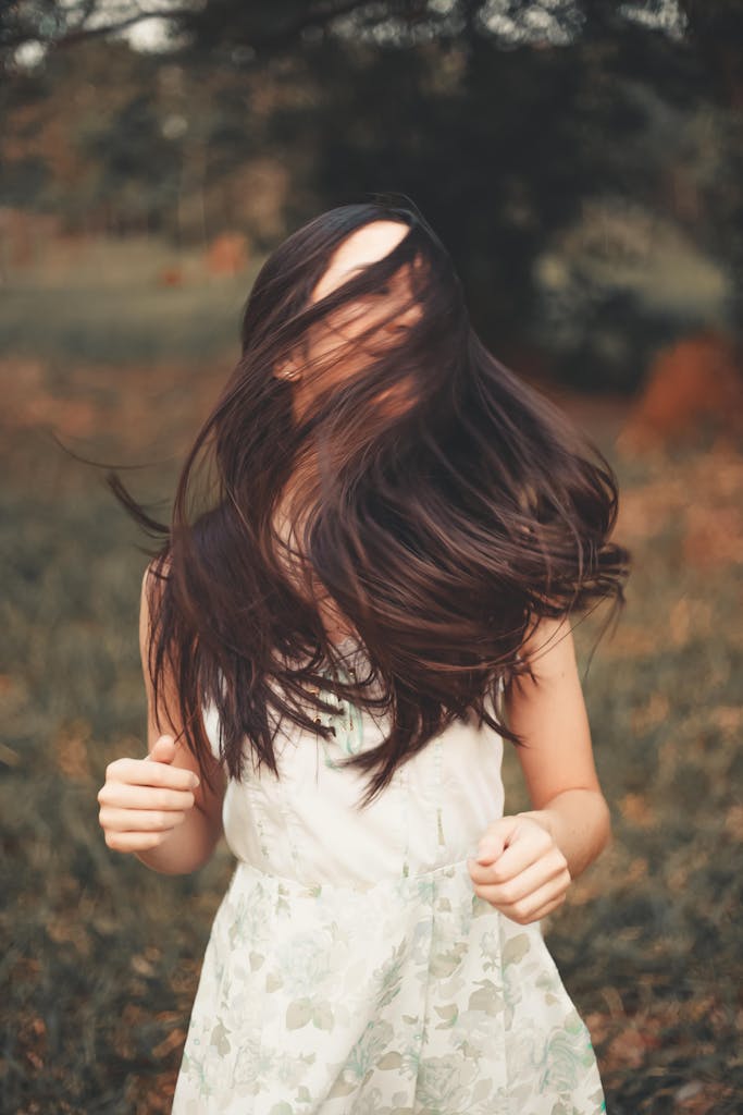 Hair loss nutrition A woman in a white dress with hair covering her face, captured in motion outdoors.