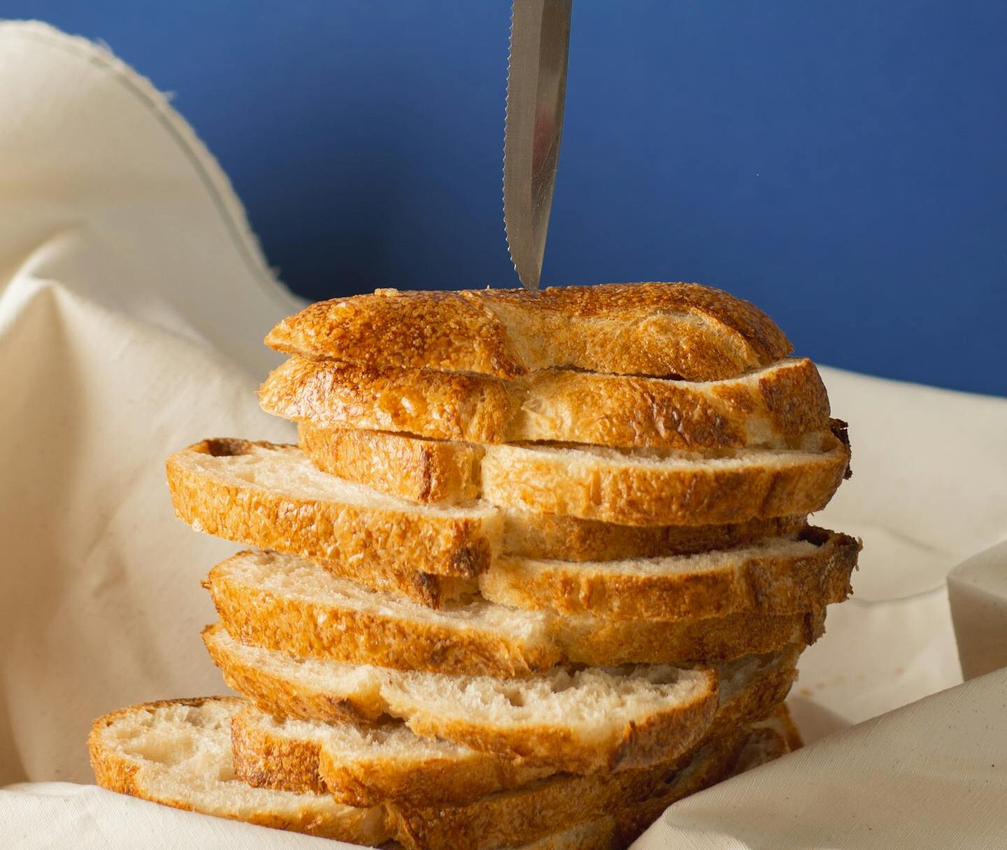Stacked slices of bread with a knife on a soft cloth against a blue backdrop in relation of eating bread in a pain when having Non-Celiac Gluten Sensitivity