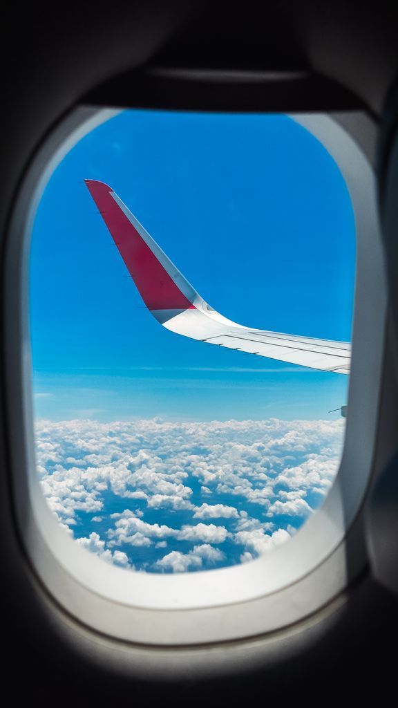 View from airplane window showing wing and clouds with clear blue sky.