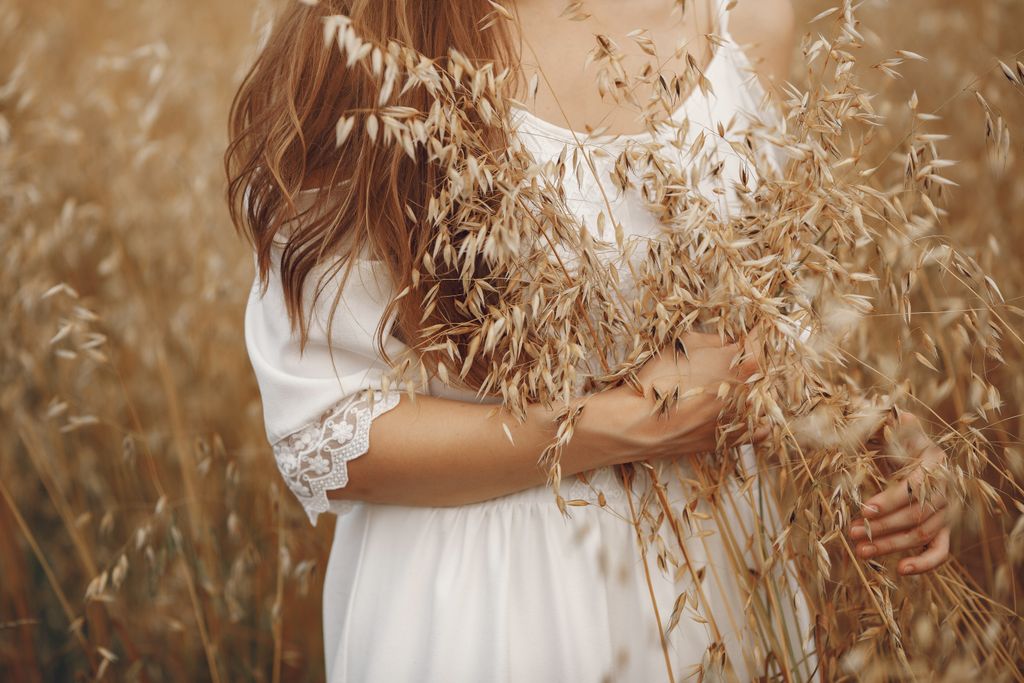 A woman in a white dress stands in a golden oat field, embracing the natural beauty of summer.