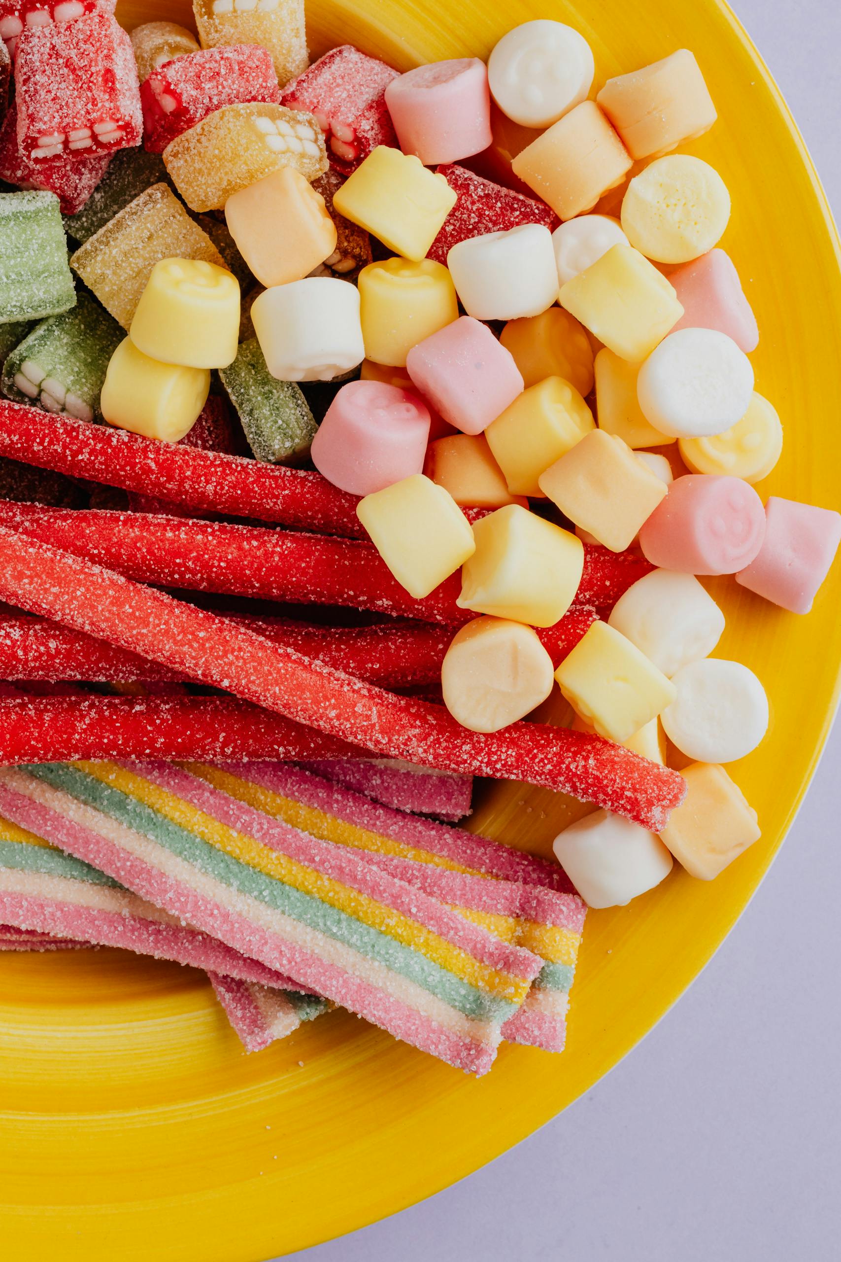 From above of set of sugary multicolored marmalade candies in yellow ceramic plate on gray background