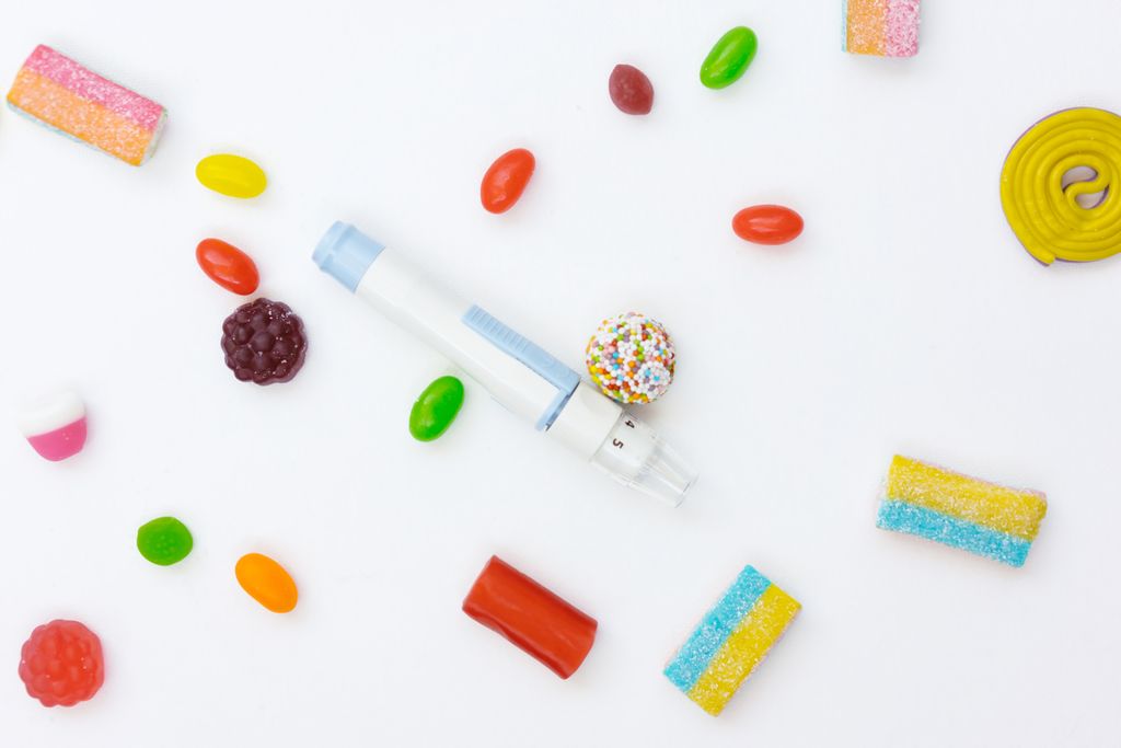 Vibrant assortment of candies surrounding an insulin pen on a white background to explain glycemic index and glycemic load