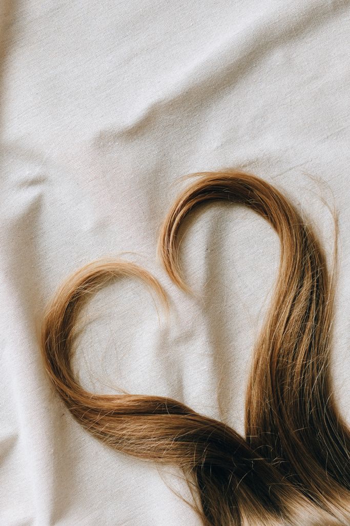 Close-up of brown hair arranged in a heart shape on soft white fabric. Healthier hair depends of the scalp microbiome.