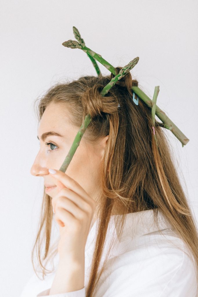 Side view portrait of a woman with asparagus in her hair against a white background.