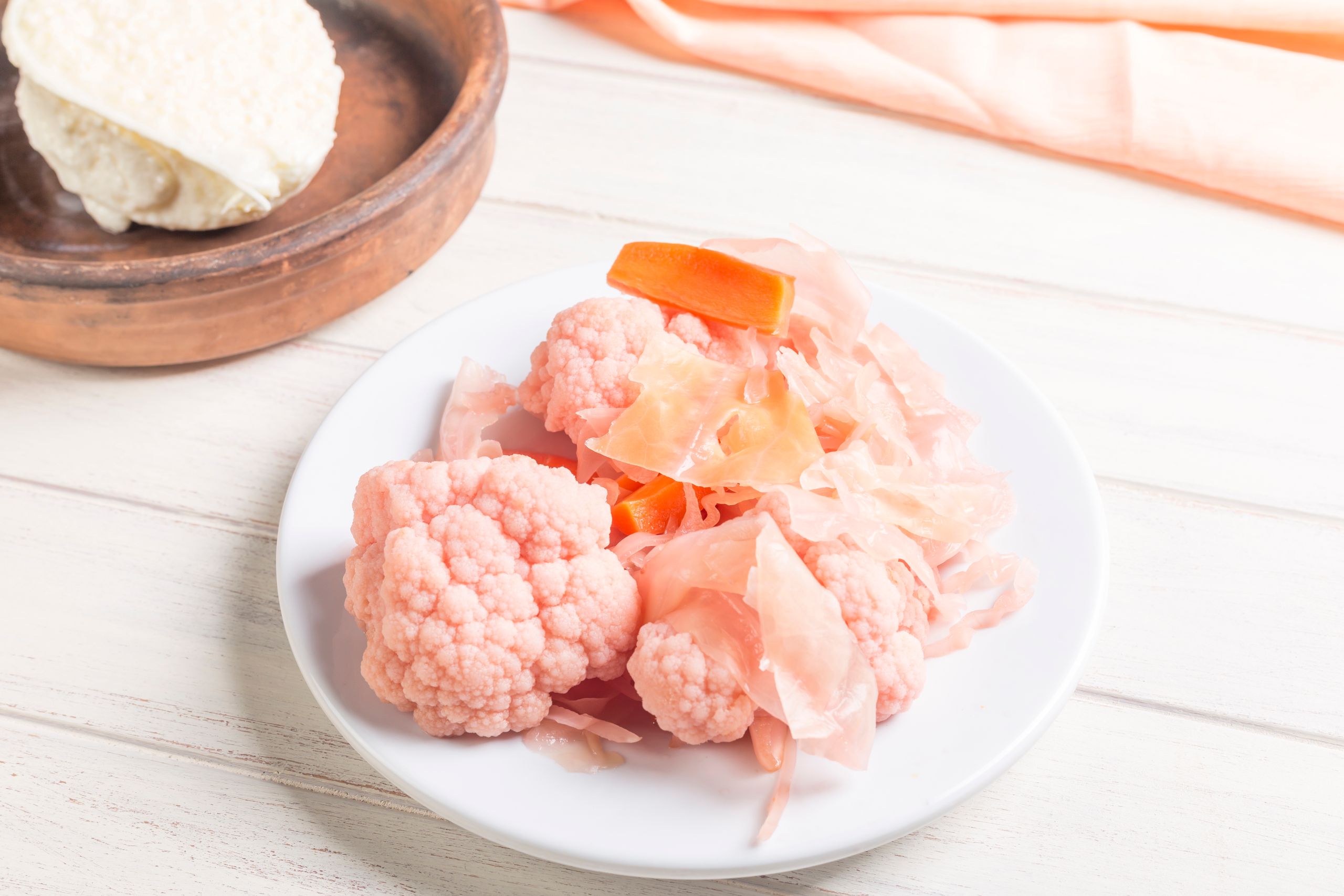 Pink fermented cauliflower and carrots on a white plate.