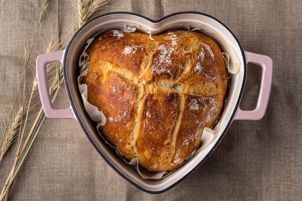 Rustic homemade bread in a heart-shaped pot on a burlap surface.