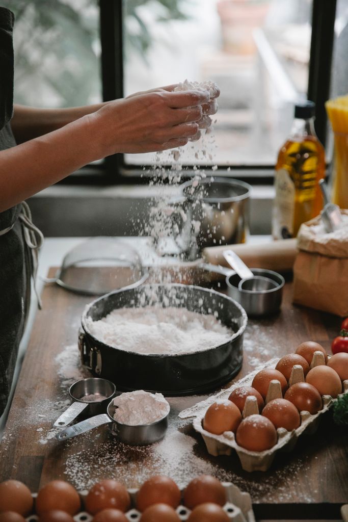 Side view of crop anonymous housewife pouring flour into baking form cooking at table with eggs oil and dishware